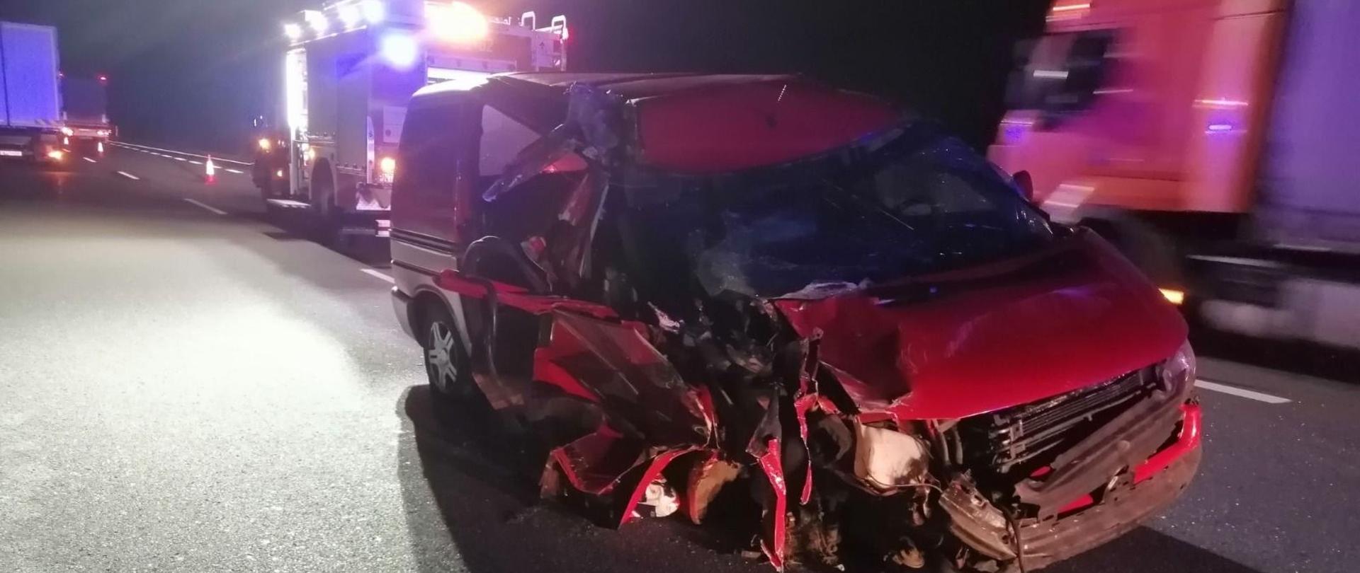 Noc. Autostrada A2, na jezdni widoczny uszkodzony samochód. W tle wóz strażacki oświetlający teren akcji.
