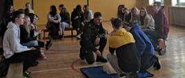 Pokaz udzielania RKO przez strażaka, wokół uczniowie, zdjęcie wykonane na sali gimnastycznej. 