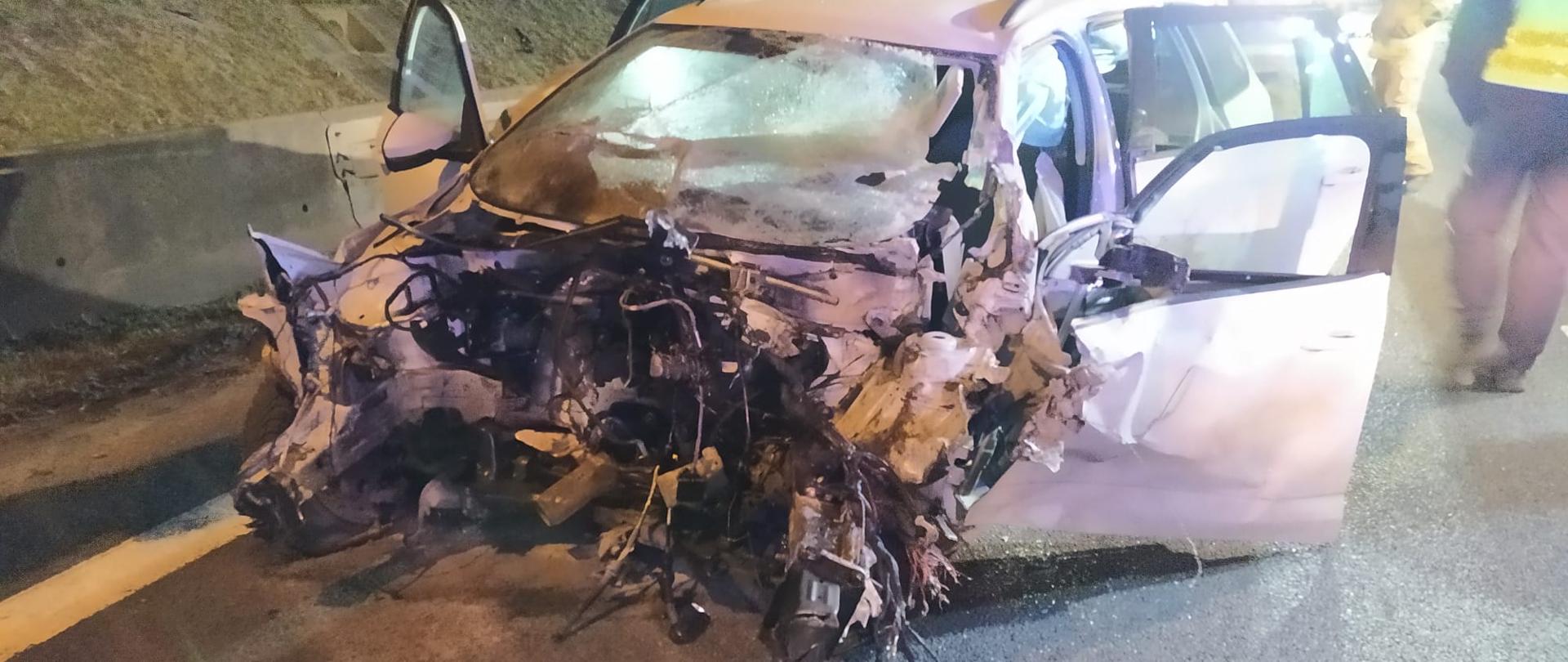 Na zdjęciu widoczny jest pojazd osobowy w kolorze białym po wypadku. Jest noc, wietrznie. 