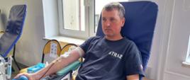 Na zajęciu widoczni strażak Ochotniczej Straży Pożarnej w granatowej koszulce i piaskowych spodniach siedzący na fotelu na sali oddający krew podczas akcji zbiórki krwi zorganizowanej przez Klub Honorowych Dawców Krwi Polskiego Czerwonego Krzyża przy Komendzie Powiatowej Państwowej Straży Pożarnej w Gorlicach.