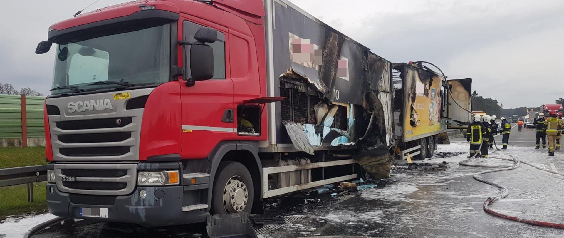 Na zdjęciu widoczna ciężarówka wraz z przyczepą w trakcie działań gaśniczych na autostradzie A4 w pobliżu Niemodlina. Po prawej stronie kadru widoczni strażacy w ubraniach specjalnych a na powierzchni jezdni widoczna pozostałość piany gaśniczej.