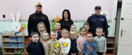 Na zdjęciu widać funkcjonariusza PSP oraz policji ubranego w ubranie służbowe w trakcie pogadanki dla uczniów szkoły
podstawowej oraz przedszkola. Znajdują się na sali.