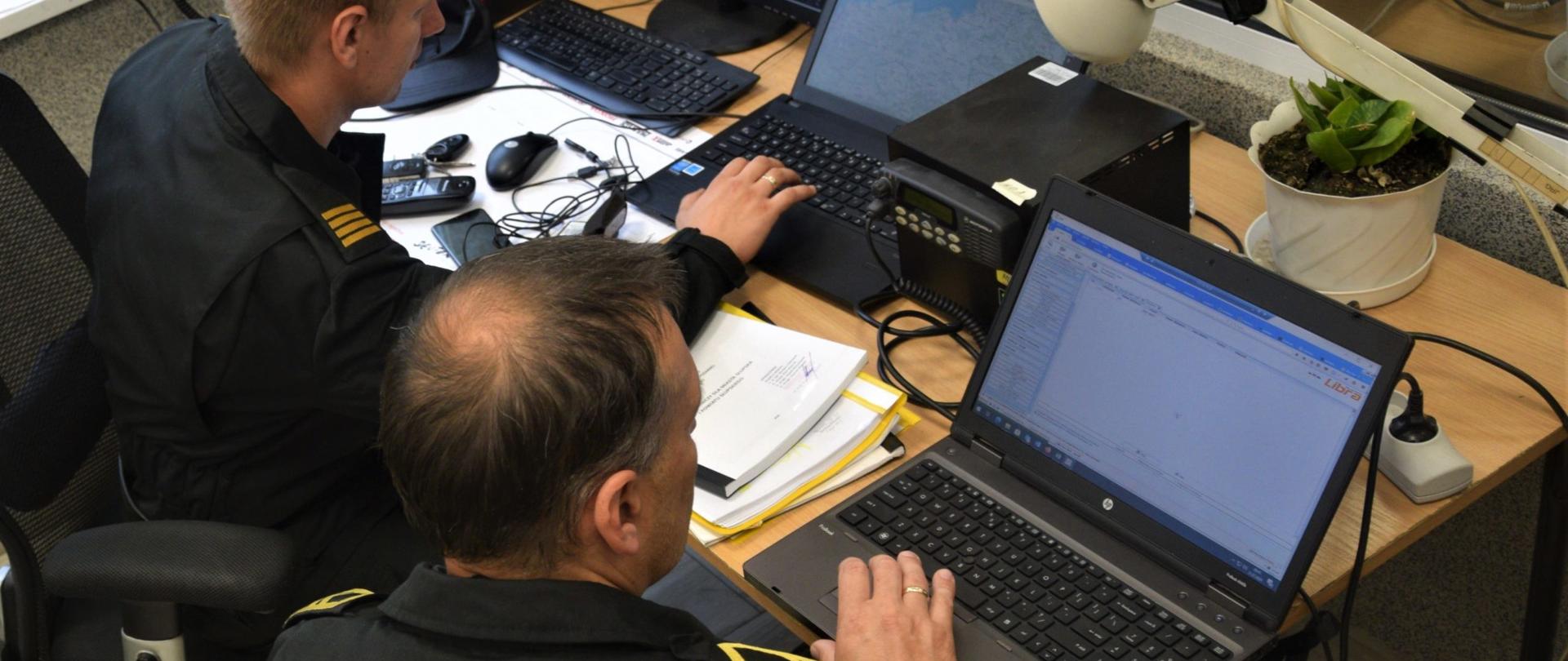 Zdjęcie przedstawia dwóch funkcjonariuszy pracujących przy komputerach na zapasowym stanowisku kierowania.