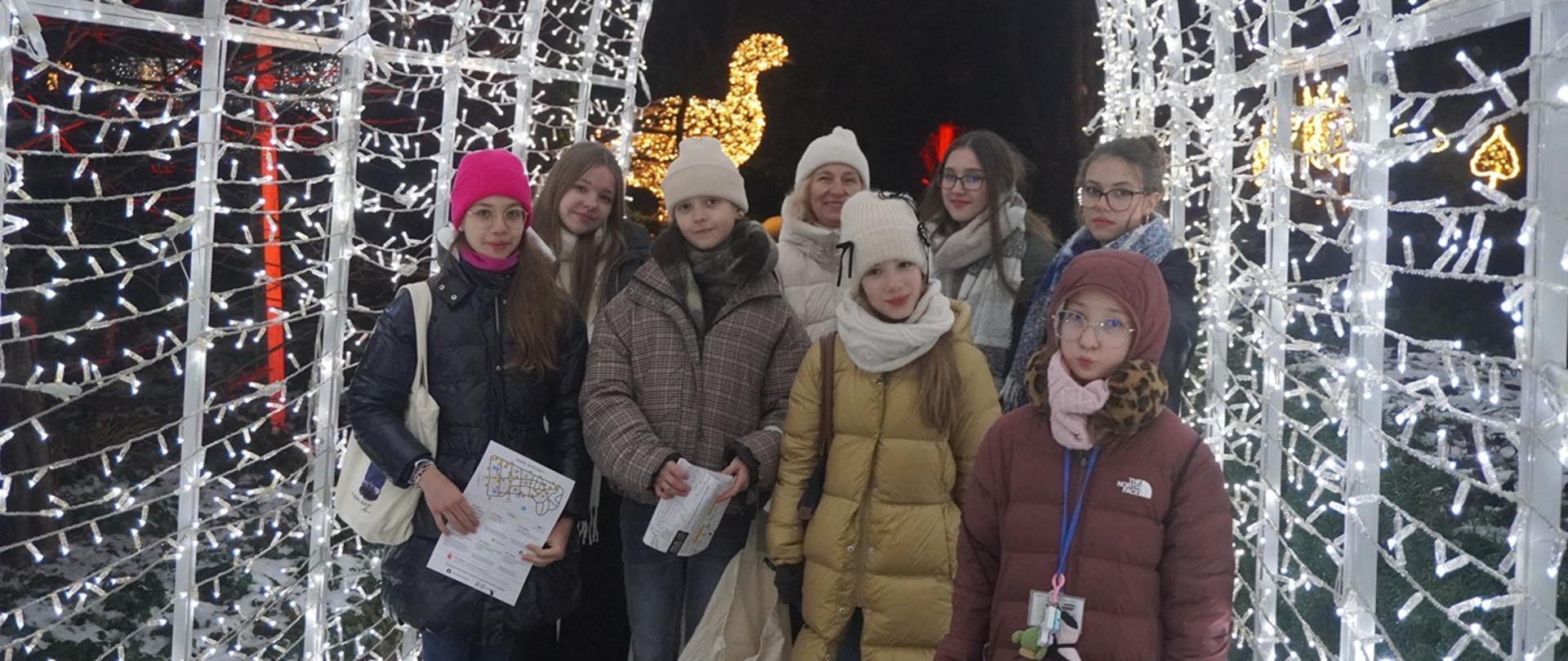 Wychowanki pozują do grupowego zdjęcia na tle iluminacji Ogrodu Botanicznego