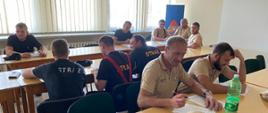 Na zdjęciu widać strażaków w trakcie zaliczania części teoretycznej egzaminu w sali szkoleniowej.