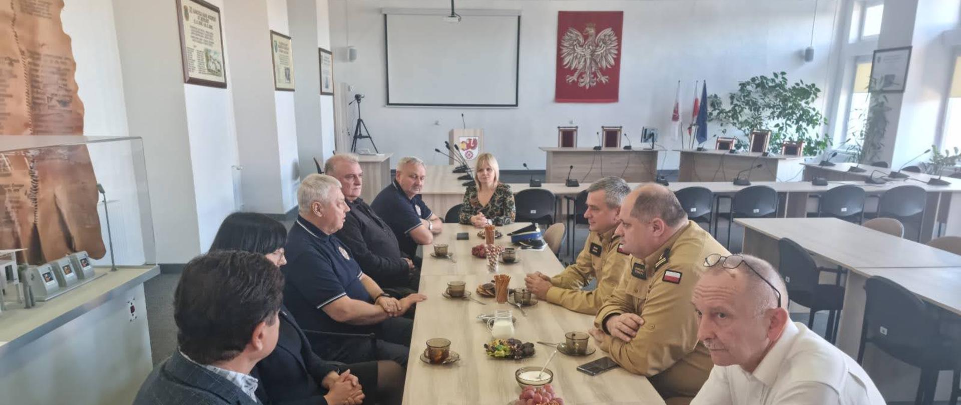 Strażacy Państwowej Straży Pożarnej, władze samorządowe siedzą przy stole rozmawiając na temat ochrony przeciwpożarowej.