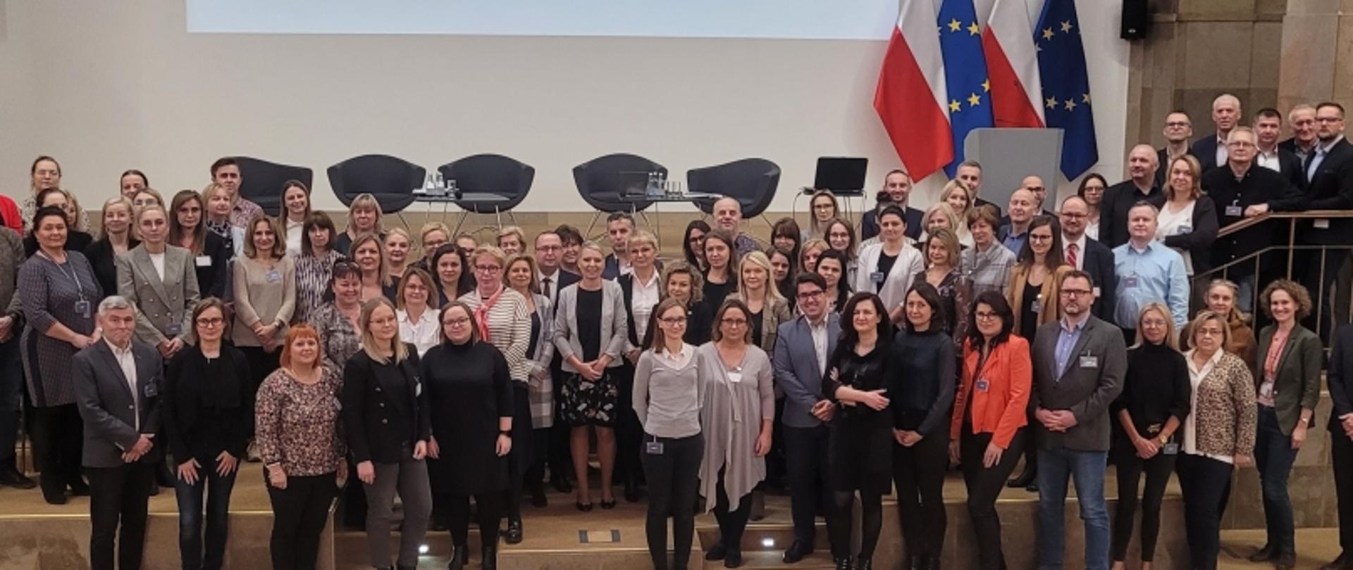 Grupowe zdjęcie uczestników wydarzenia w formalnym otoczeniu.