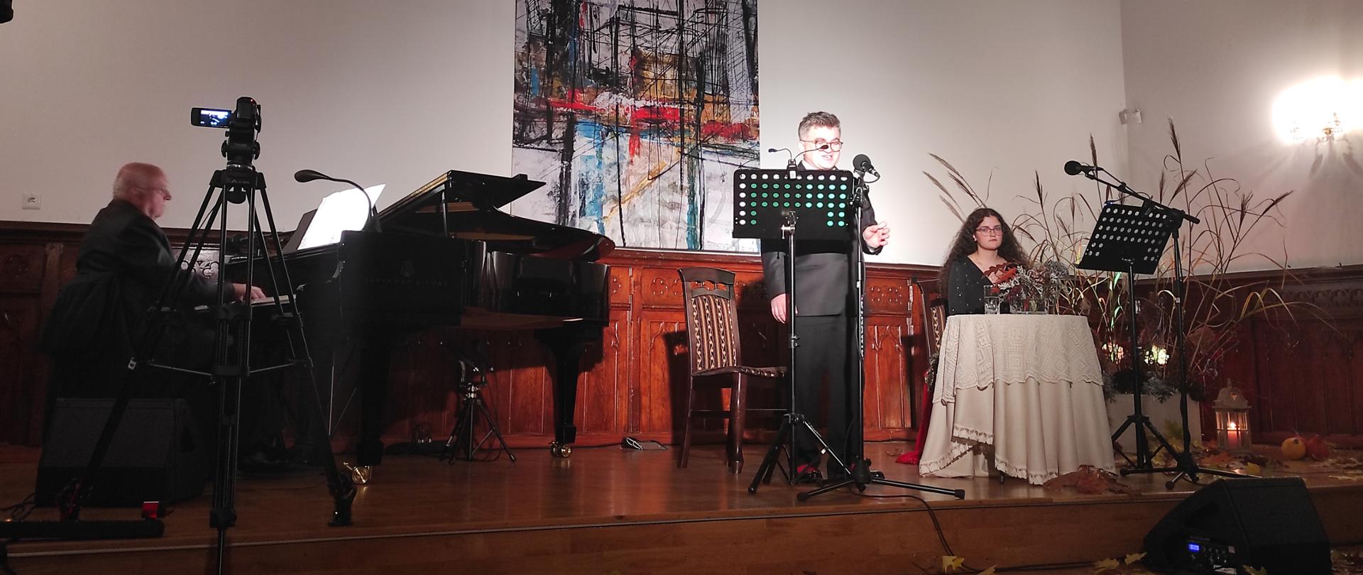 zdjęcie przedstawia wykonawców koncertu "refleksje" na scenie w sali królewskiej Państwowej Szkoły Muzycznej w Mielcu, od lewej strony, przy fortepianie Tadeusz Wywrocki, następnie solista Marcin Pokusa, obok niego Magdalena Kopacz