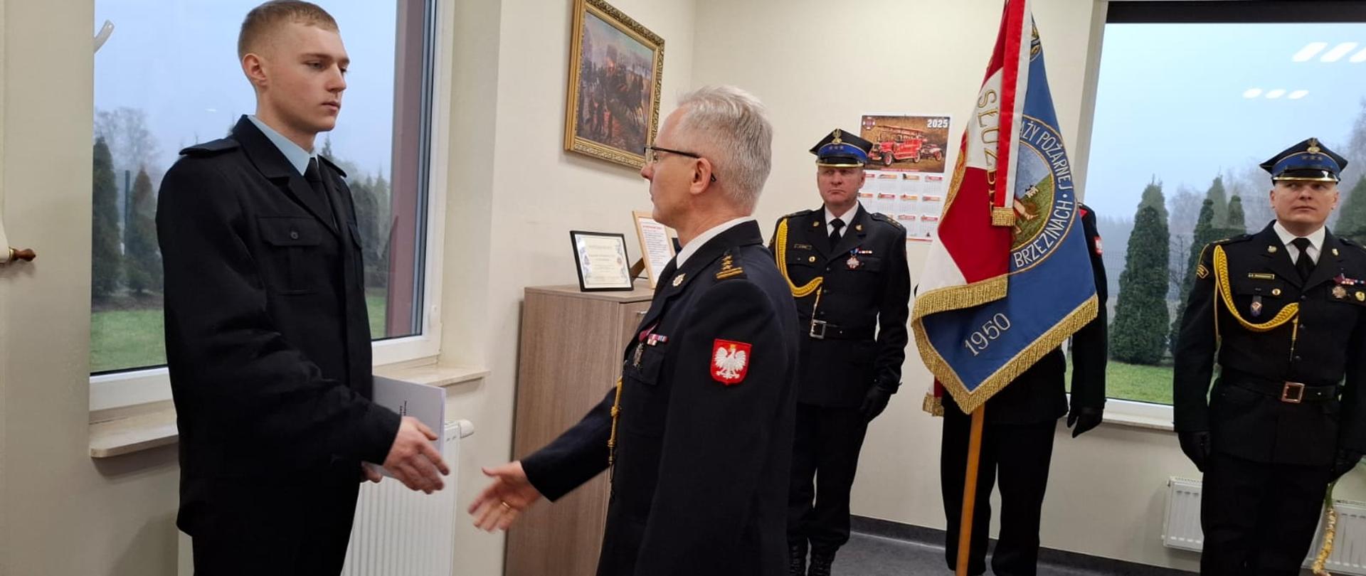 Komendant Powiatowy Państwowej Straży Pożarnej w Brzezinach starszy brygadier Mariusz Kaczmarski wręcza podpisany Akt Ślubowania nowo przyjętemu strażakowi.