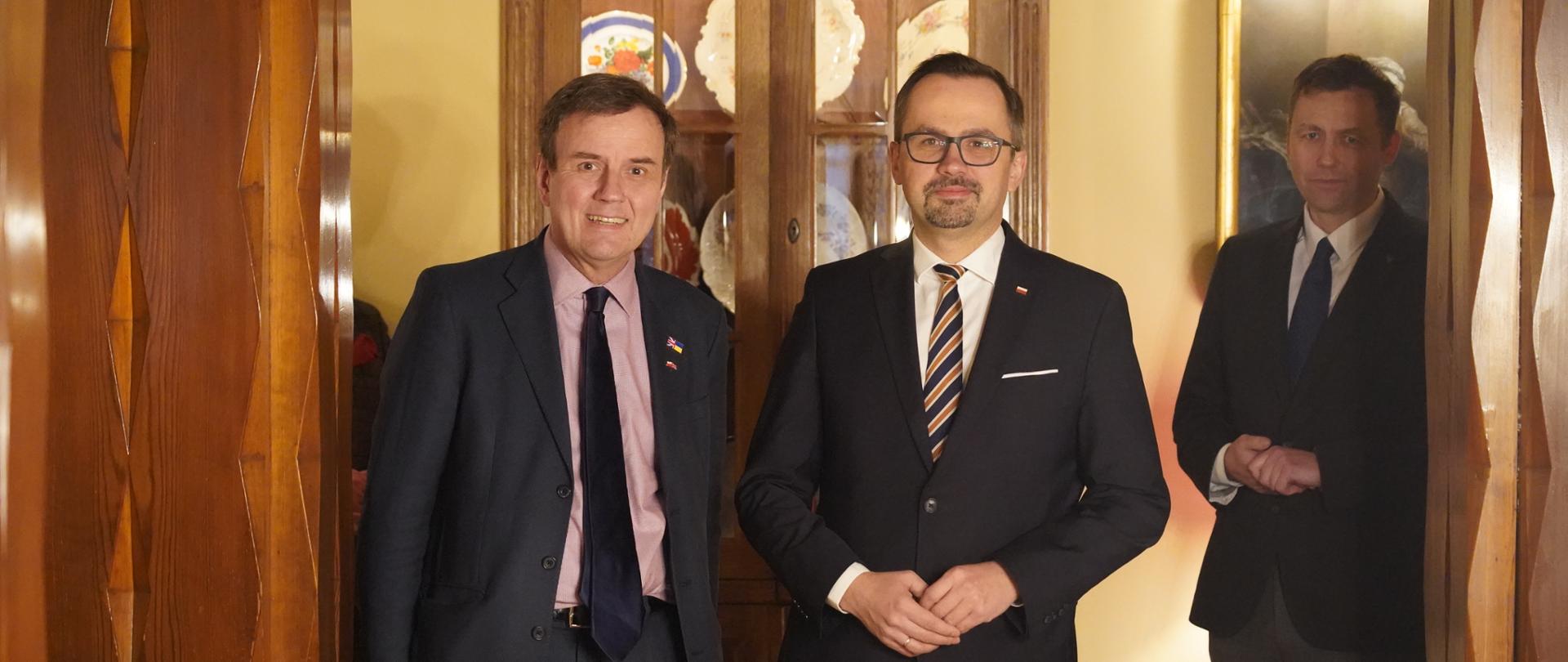 Trzech mężczyzn stoi obok siebie. Dwóch bardziej z przodu, trzeci nieco z tyłu. W środku jest wiceminister Marcin Horała.