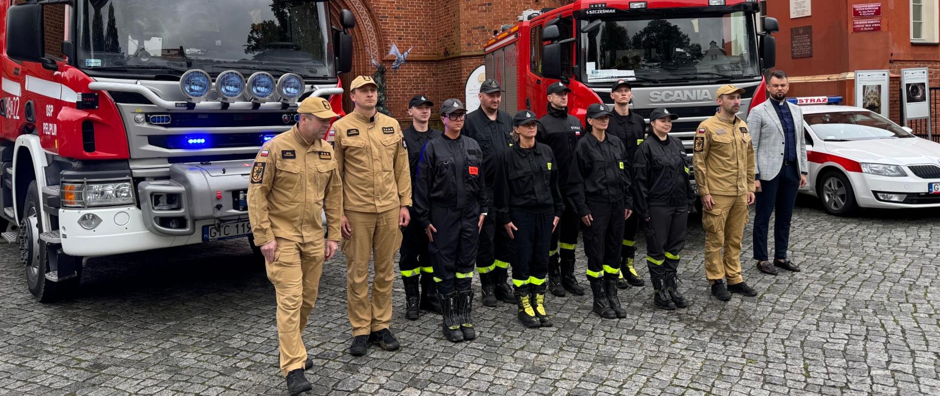 Strażacy i zaproszeni goście stoją przed wozami strażackimi i katedrą w Pelplinie podczas uroczystości rocznicowych 11 września.