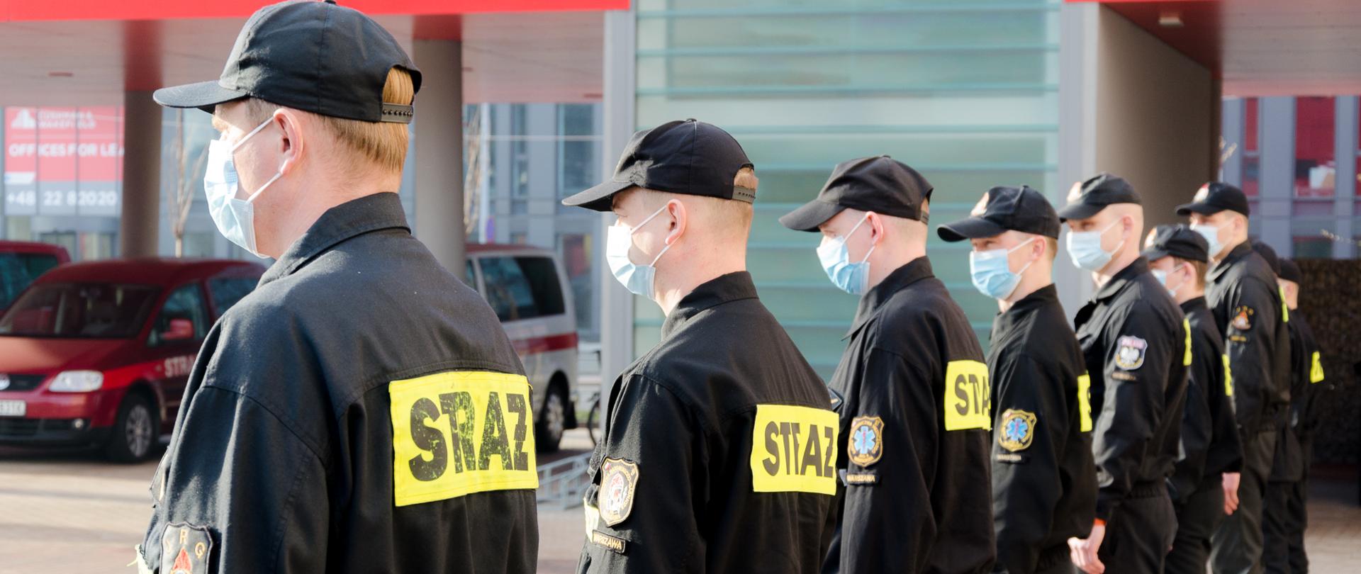 Na zdjęciu strażacy na oficjalnym spotkaniu w związku delegacją do Centralnego Szpitala Klinicznego MSWiA. Strażacy ubrani w mundury koszarowe koloru czarnego. 