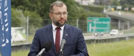Minister funduszy i polityki regionalnej Grzegorz Puda stoi przed dwoma mikrofonami