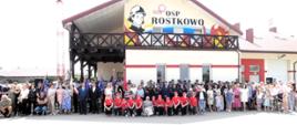 Zdjęcie grupowe uczestników wydarzenia przed budynkiem, którego szczyt zdobi mural "1926 OSP ROSTKOWO". 
