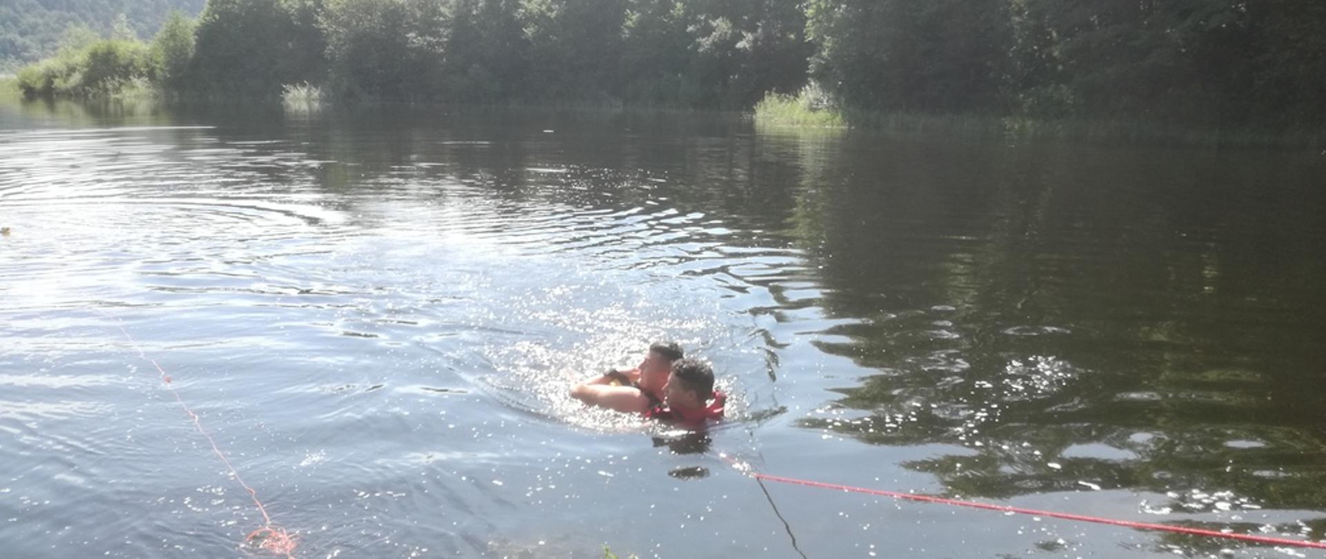 Na zdjęciu widoczni strażacy na podczas ćwiczeń z zakresu ratownictwa wodnego na zalewie Klimkówka jeden ze strażaków ewakuuje osobę tonącą z wody.