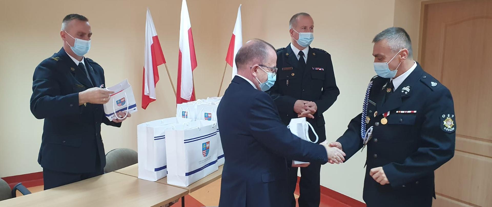 Zdjęcie przedstawia wicemarszałka województwa świętokrzyskiego Marka Bogusławskiego wraz z komendantem powiatowym Państwowej Straży Pożarnej st. bryg. Pawłem Jakubowskim oraz jego zastępcą bryg. Tomaszem Szymańskim, którzy przekazują pulsoksymetry przedstawicielom OSP.