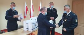 Zdjęcie przedstawia wicemarszałka województwa świętokrzyskiego Marka Bogusławskiego wraz z komendantem powiatowym Państwowej Straży Pożarnej st. bryg. Pawłem Jakubowskim oraz jego zastępcą bryg. Tomaszem Szymańskim, którzy przekazują pulsoksymetry przedstawicielom OSP.