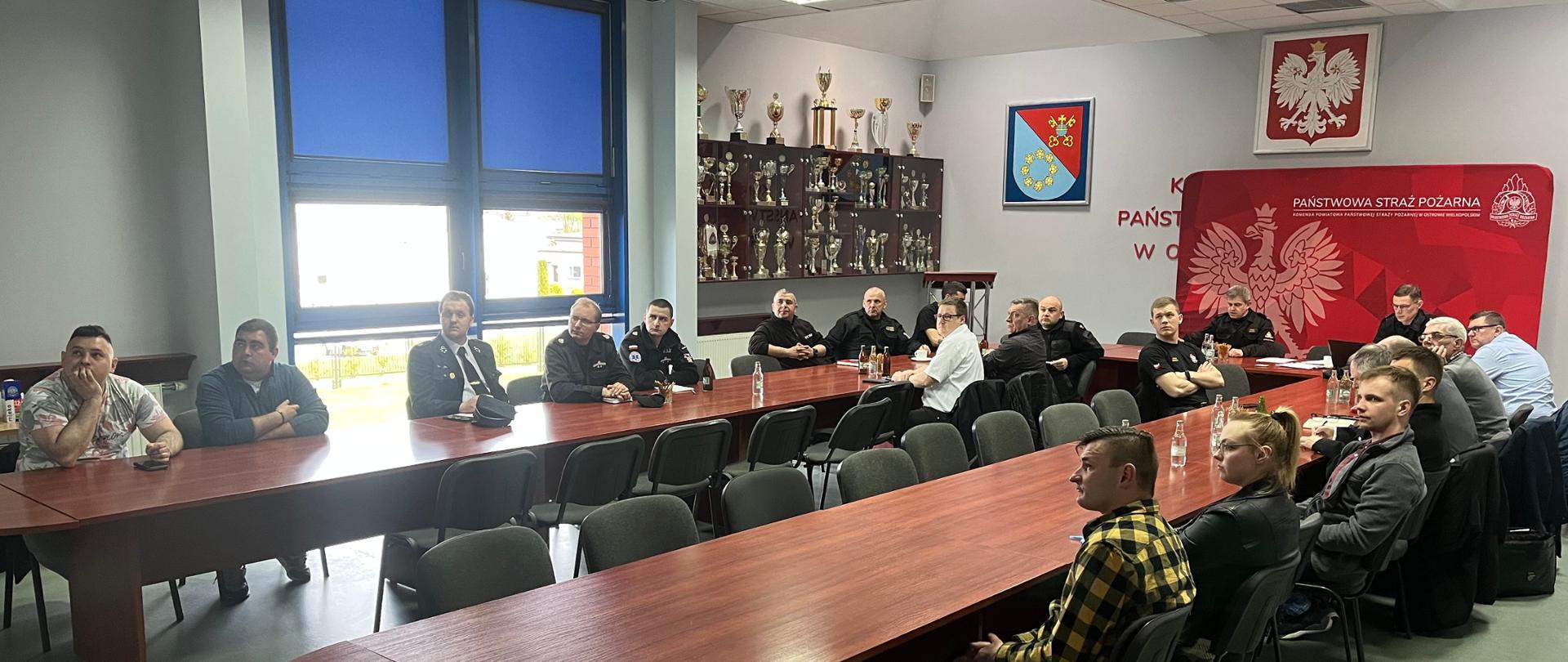 Uczestnicy spotkania - strażacy siedzą na sali konferencyjnej i patrzą na prezentację wyświetloną na ścianie przez projektor.