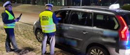 Nocna kontrola taksówki na jednym z postojów w Szczecinie. Funkcjonariusze ITD stoją obok pojazdu oznakowanego jako taksówka i pobierają wymagane dokumenty od kierującego.