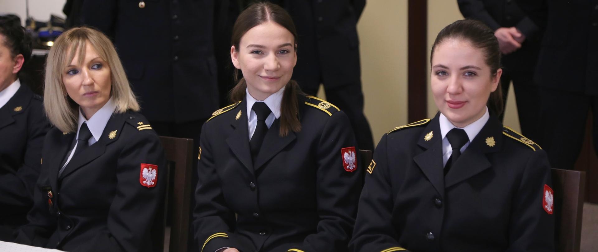 Funkcjonariuszka CS PSP oraz dwie kadetki w mundurach galowych siedzące przy stole