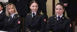 Funkcjonariuszka CS PSP oraz dwie kadetki w mundurach galowych siedzące przy stole