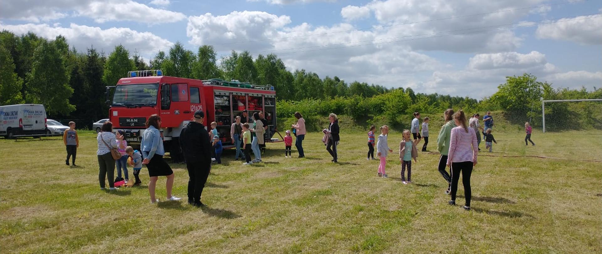 Na boisku sportowym dzieci zgromadzone wokół wozu strażackiego