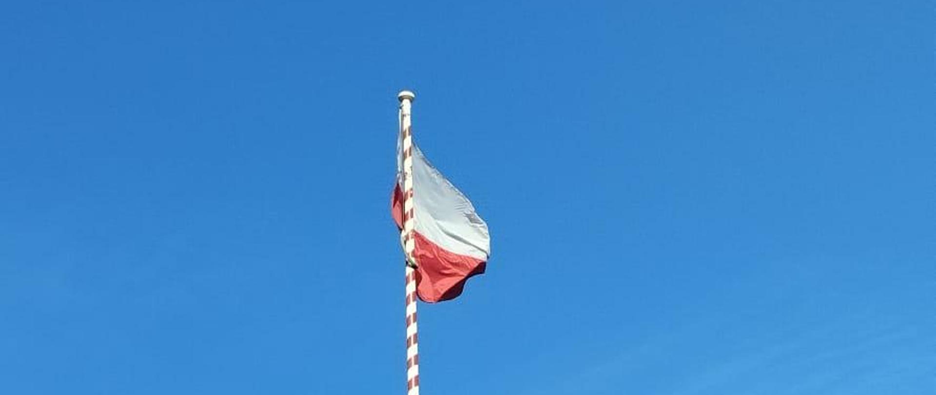 Zdjęcie przedstawia funkcjonariuszy KP PSP podczas uroczystej zmiany służby i podniesienia flagi państwowej RP na maszt.