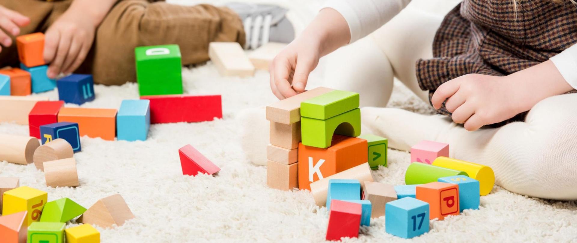 Na zdjęciu widać chłopca i dziewczynkę bawiących się klockami na dywanie.