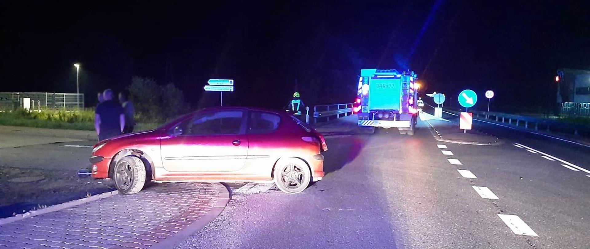 Samochód osobowy stoi częściowo na chodniku a częściowo na drodze.