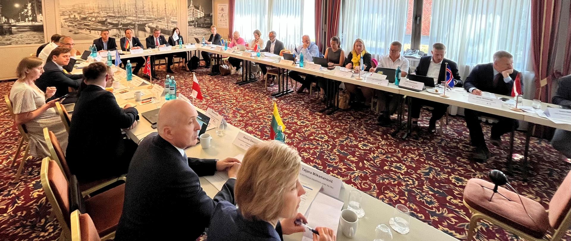 W sali konferencyjnej przy stole w kształcie litery U siedzą uczestnicy spotkania