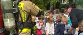 Zdjęcie przedstawia strażaka prezentującego aparat ochrony układu oddechowego. Dookoła znajdują się dzieci.
