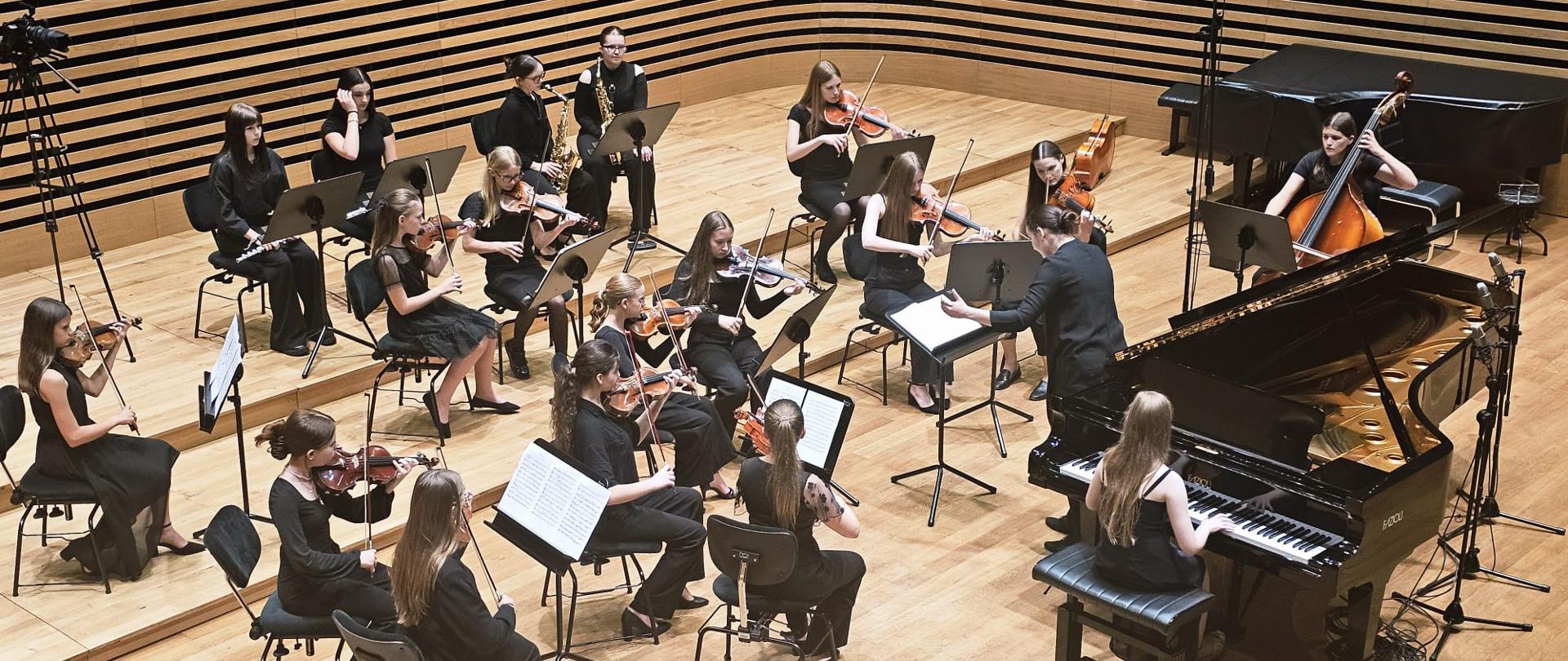 Dziewczyna gra na fortepianie, kobieta dyryguje orkiestrą.