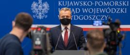 Wojewoda Mikołaj Bogdanowicz rozmawia z dziennikarzami. Maseczka