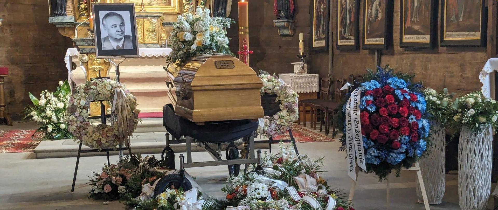 trumna na tle ołtarza a wokół wieńce z kwiatów 