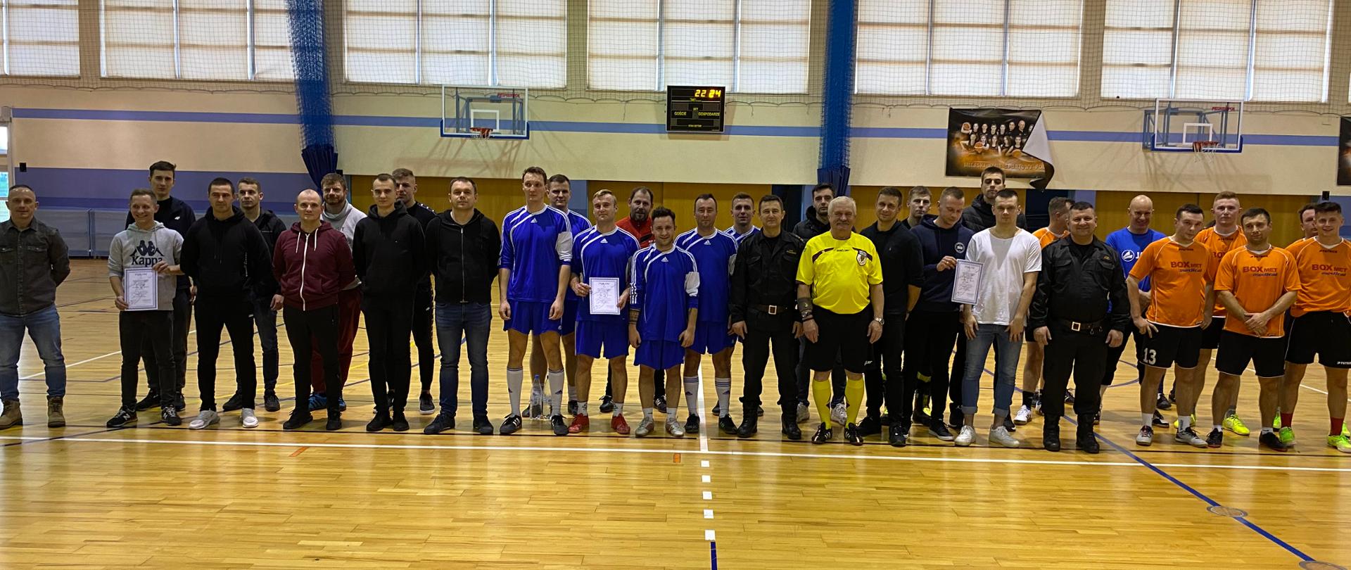 Fotografia przedstawia strażaków biorących udział w zawodach w sali gimnastycznej