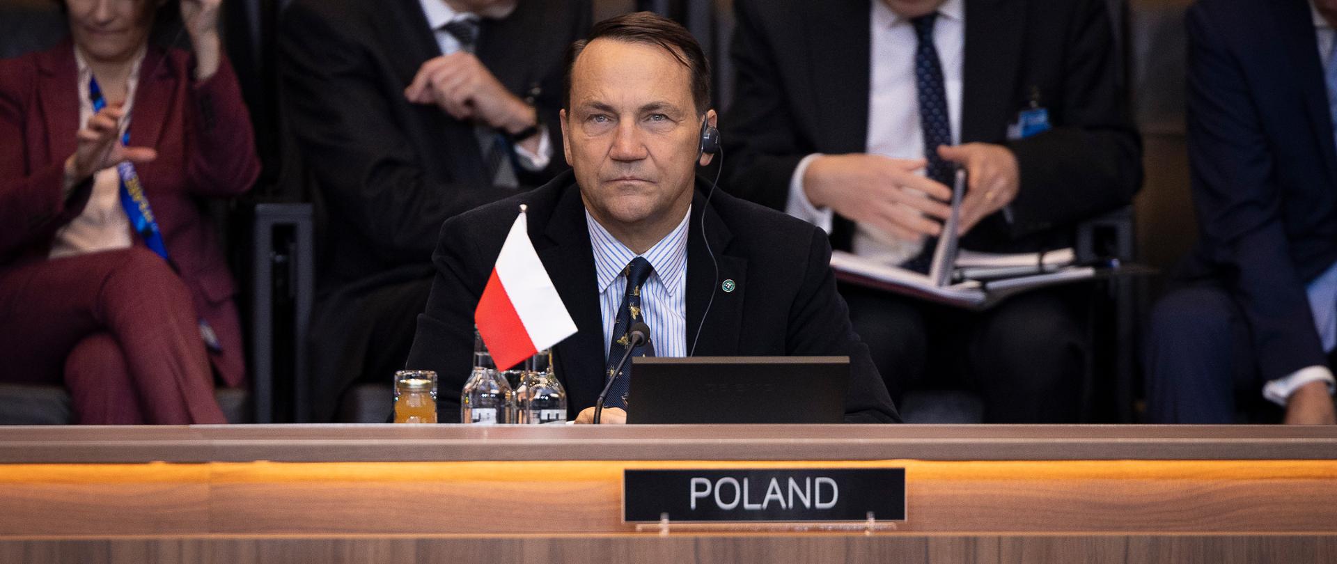 Wicepremier Radosław Sikorski na sali posiedzeń NATO za tabliczką z napisem Polska