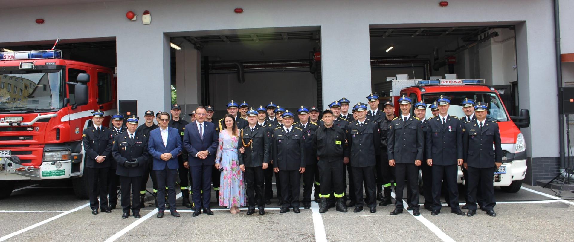 Na zdjęciu na tle otwartych garaży strażnicy ustawieni w szeregu stoi kilkudziesięciu strażaków i zaproszonych gości.