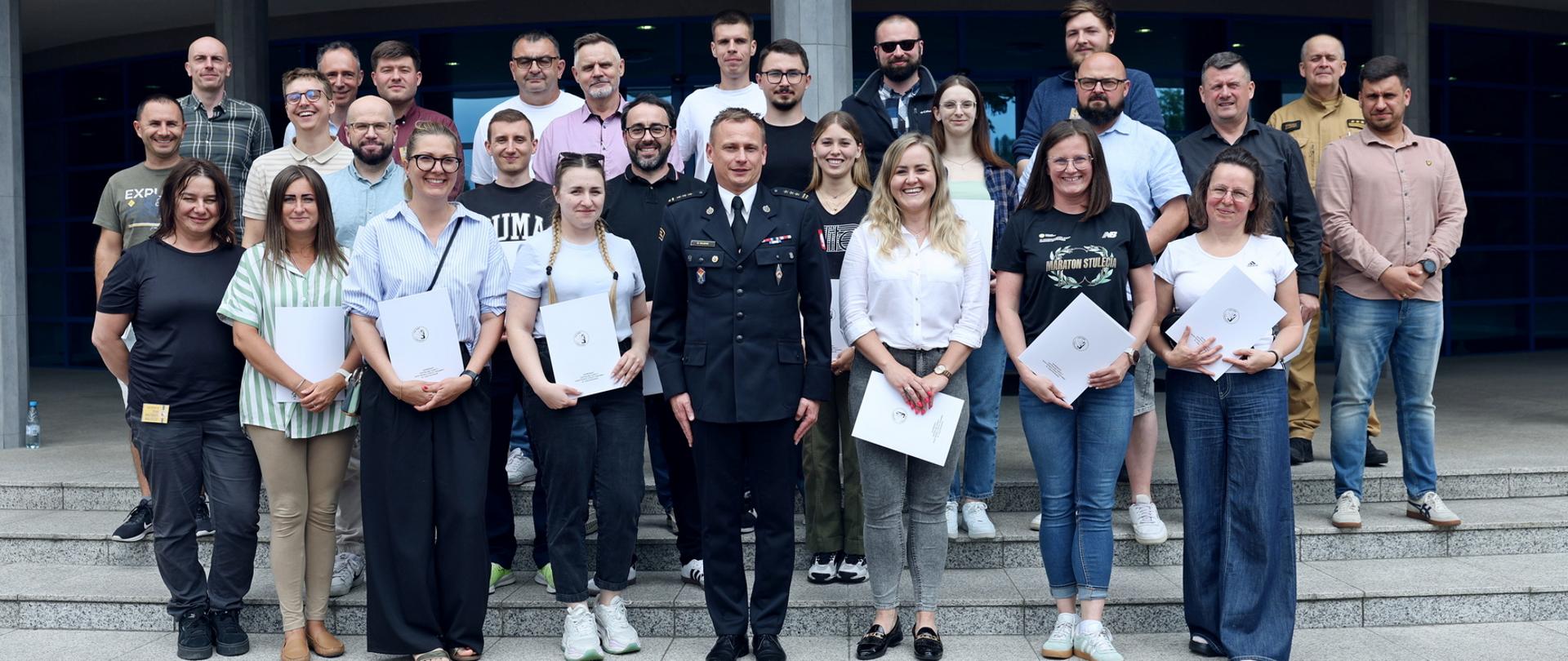 Pamiątkowe zdjęcie grupowe uczestników szkolenia inspektorów ochrony przeciwpożarowej (26 osób) w towarzystwie Zastępcy Komendanta Centralnej Szkoły PSP oraz funkcjonariusza CS PSP