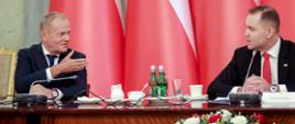 Premier Donald Tusk i Prezydent Karol Nawrocki podczas posiedzenia Rady Gabinetowej 27.08.2025 r. W tle biało-czerwone flagi.
