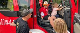 Dzieci w asyście strażaka siedzą w kabinie wozy strażackiego