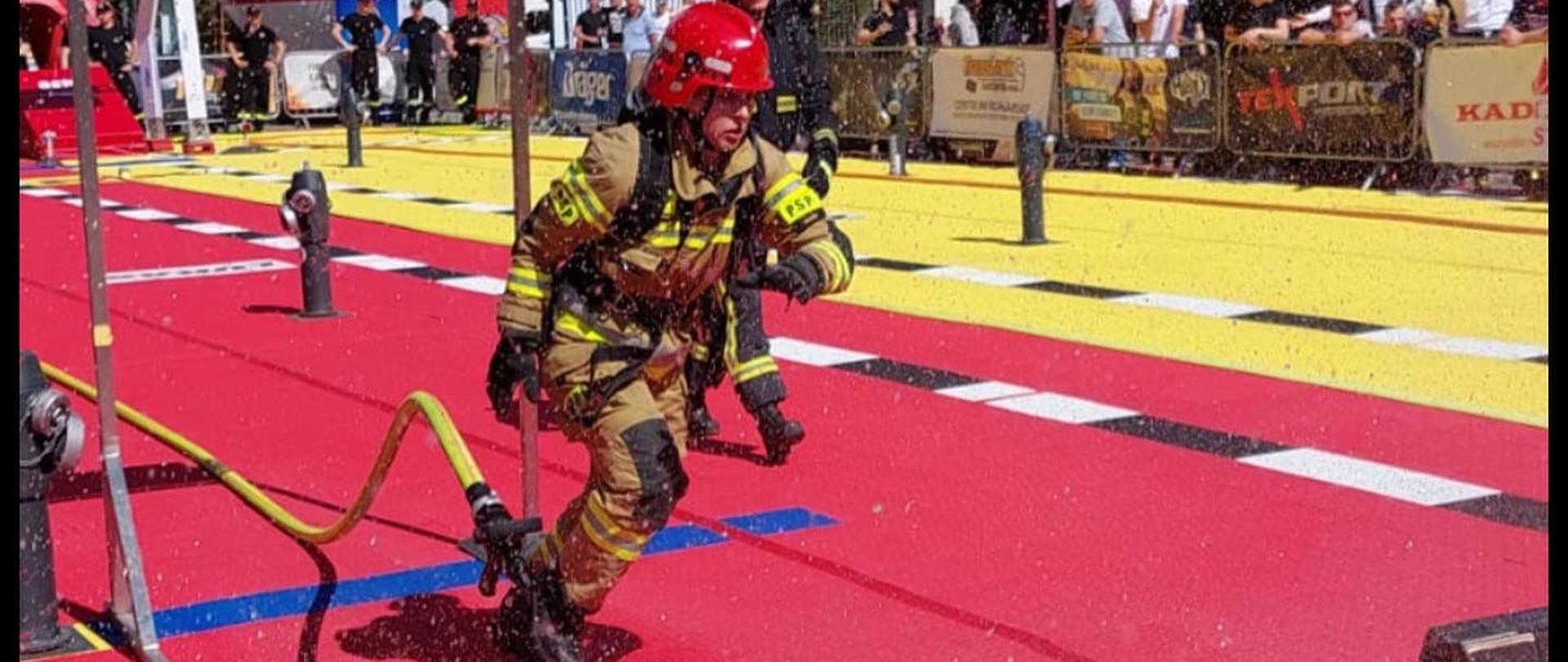 Na zdjęciu strażak podczas biegu na torze za przeszkodą ubrany w ubranie specjalne 
