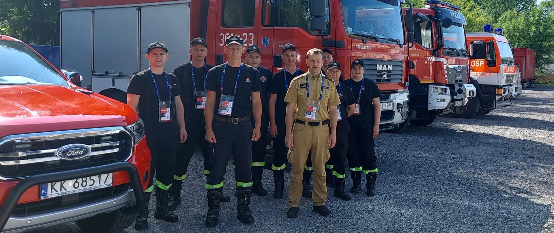 Na zdjęciu widoczni strażacy na tle samochodów pożarniczych.