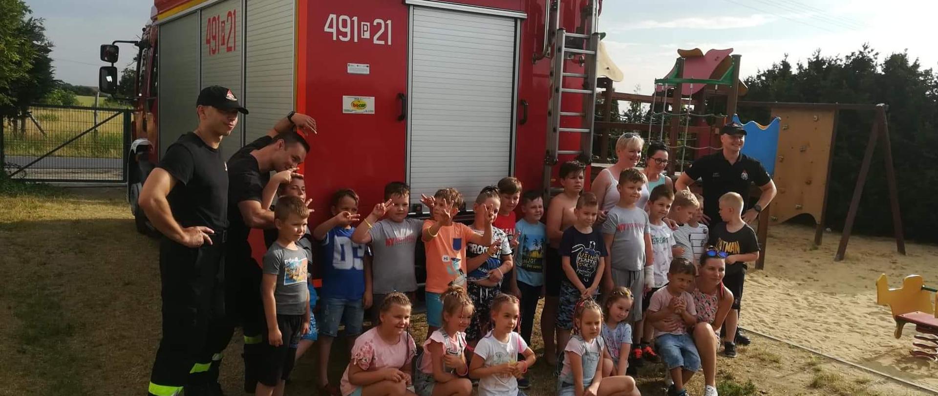 Zdjęcie grupowe na tle pojazdu pożarniczego. Na zdjęciu strażacy, opiekunowie oraz grupa najmłodszych pociech. 