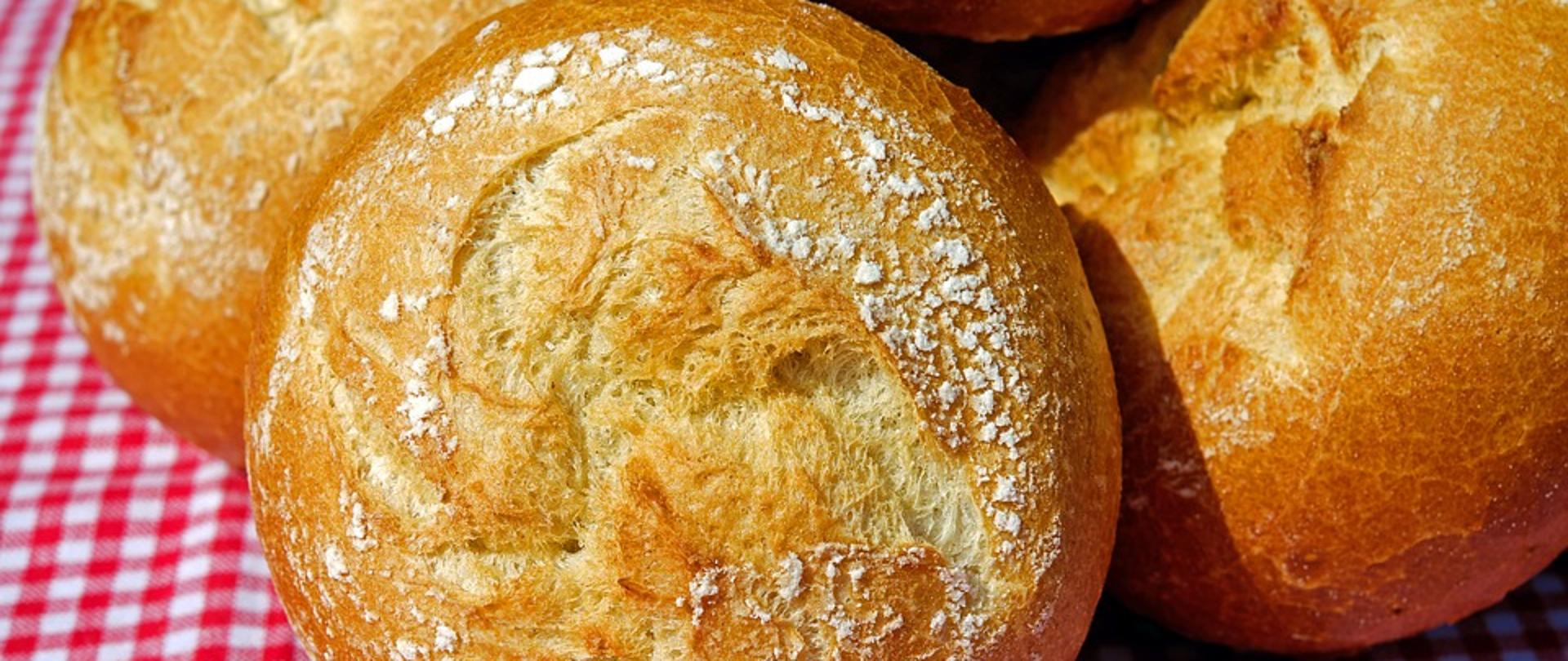 Na środku zdjęcia znajdują się trzy bułki leżące na obrusie. 