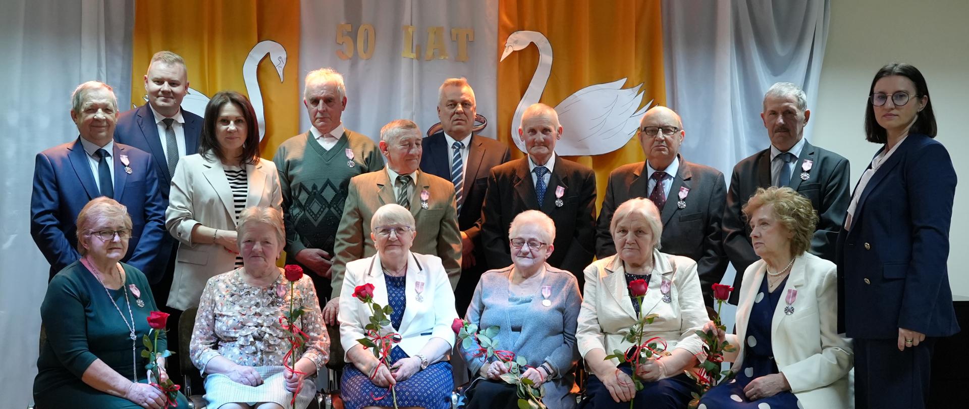 Na zdjęciu grupa ludzi. Kobiety trzymają w dłoniach czerwone róże. 