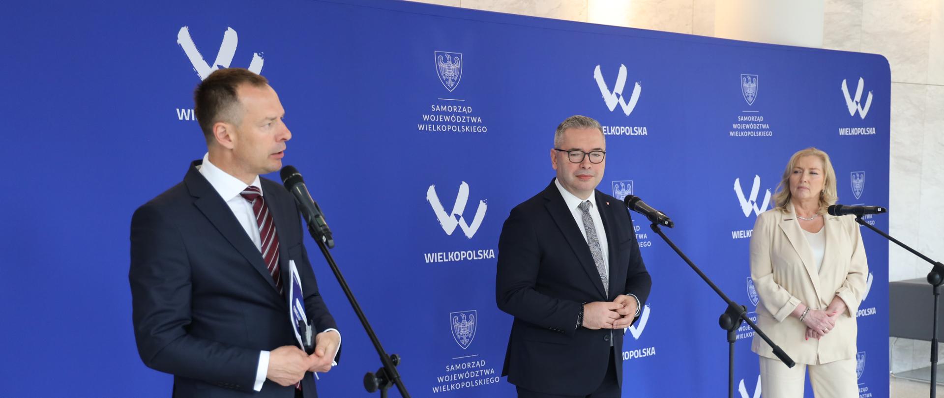Konferencja nt. rozwoju turystyki w Poznaniu. Za mikrofonem stroi Piotr Borys oraz dwie inne osoby. Stoją na tle niebieskiej ścianki z logiem województwa wielkopolskiego