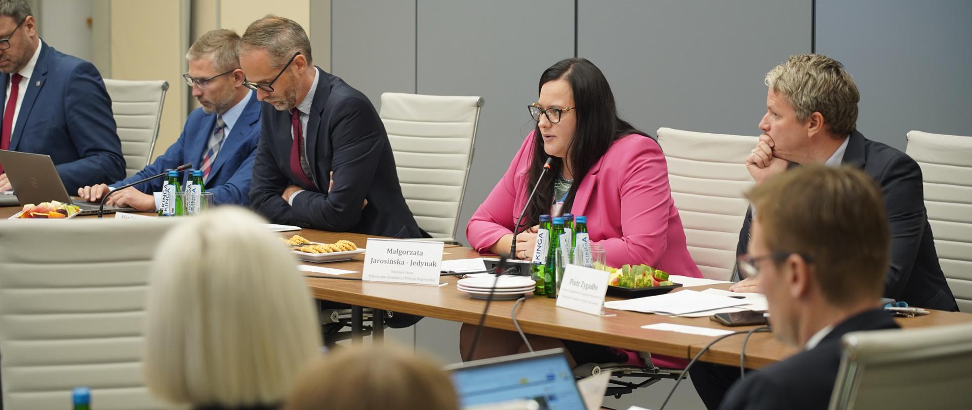 Grupa osób w sali konferencyjnej siedzi przy stołach. Wśród nich wiceminister Małgorzata Jarosińska-Jedynak.