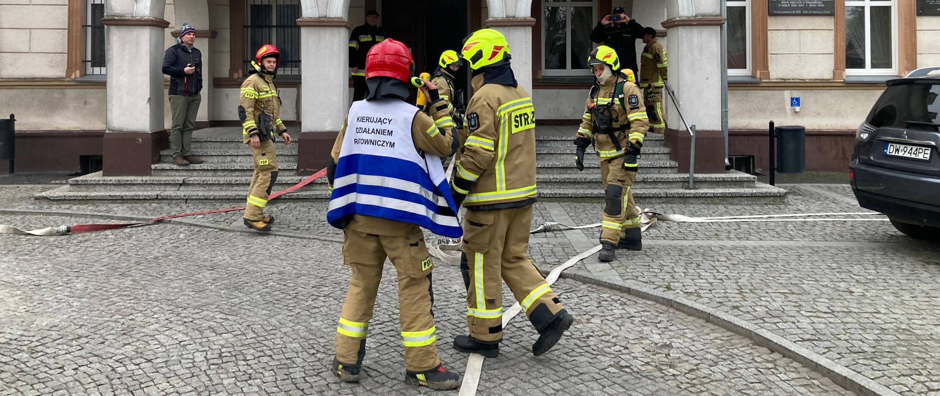 Zdjęcie przedstawia strażaków przed wejściem do pałacu. W tle znajduje się pałac.