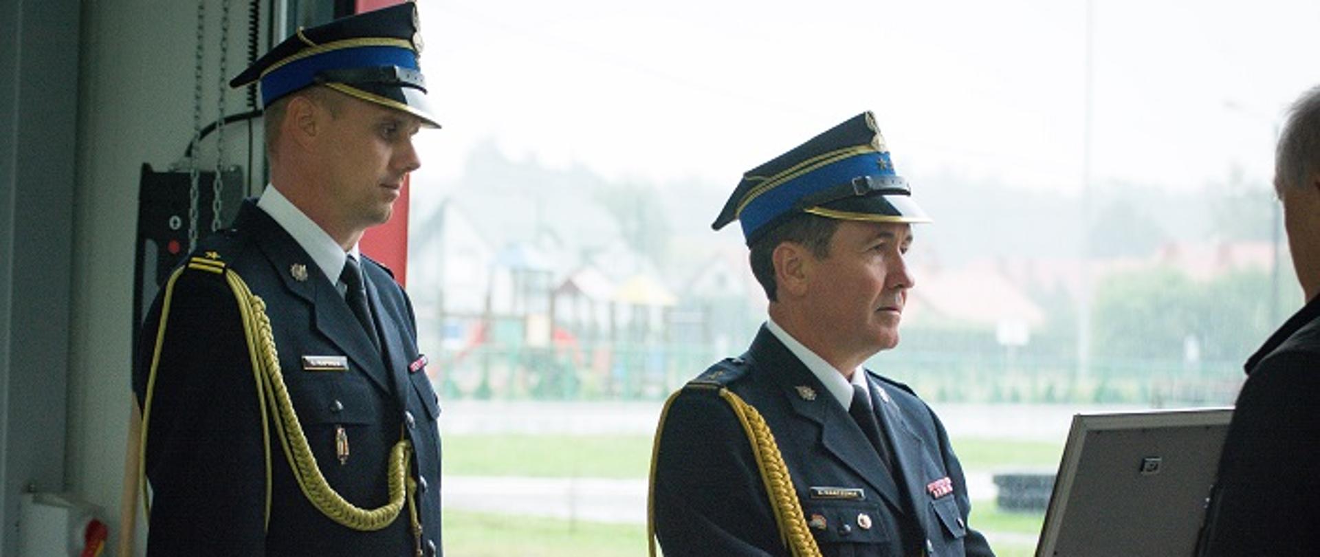 Fotografia przedstawia w umundurowaniach galowych: zastępce podkarpackiego komendanta wojewódzkiego Państwowej Straży Pożarnej bryg. Andrzeja Marczenię i stojącego obok komendanta powiatowego Państwowej Straży Pożarnej w Mielcu mł.bryg. Łukasza Kapinosa. Zastępca podkarpackiego komendanta wojewódzkiego w rękach trzyma decyzję oprawioną w ozdobną ramkę o włączeniu jednostki do krajowego systemu ratowniczo gaśniczego. 