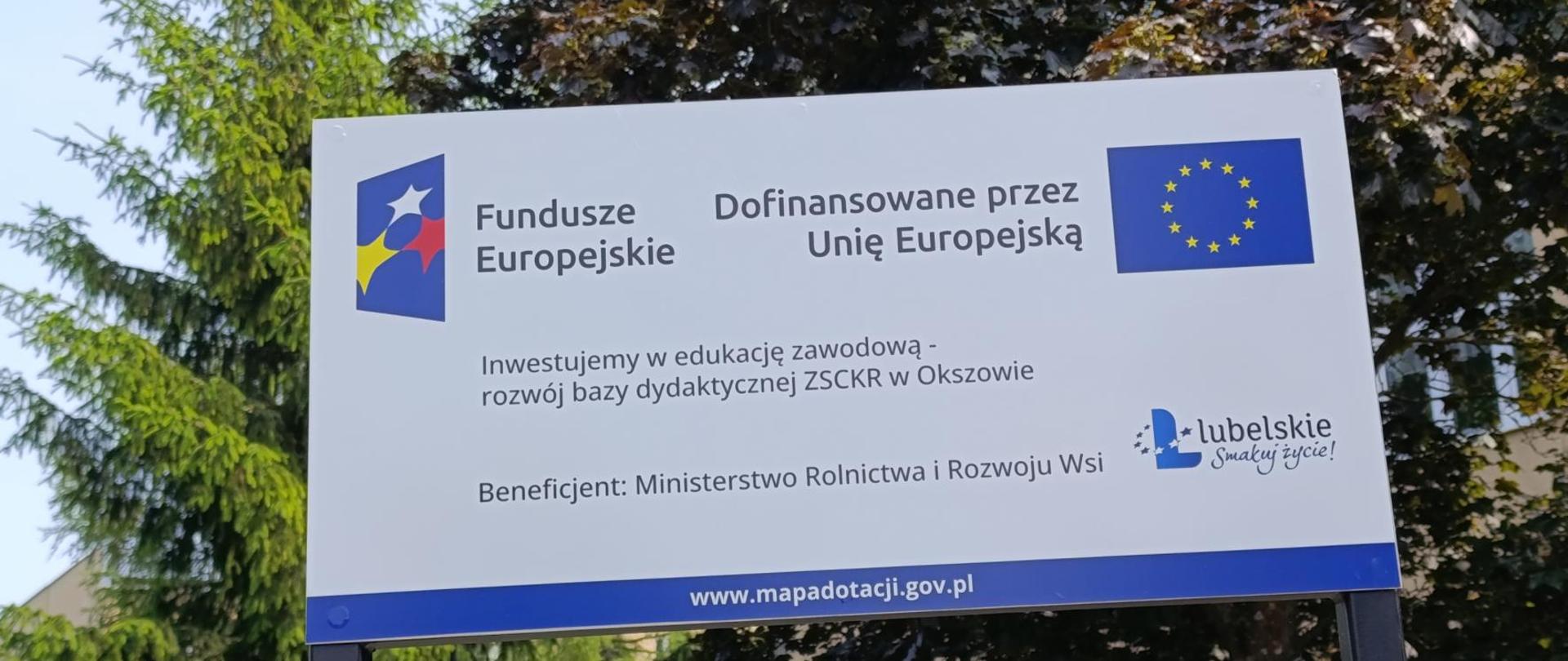 Tablica informacyjna Funduszy Europejskich przy ZSCKR w Okszowie, informująca o dofinansowaniu rozwoju bazy dydaktycznej przez Unię Europejską.